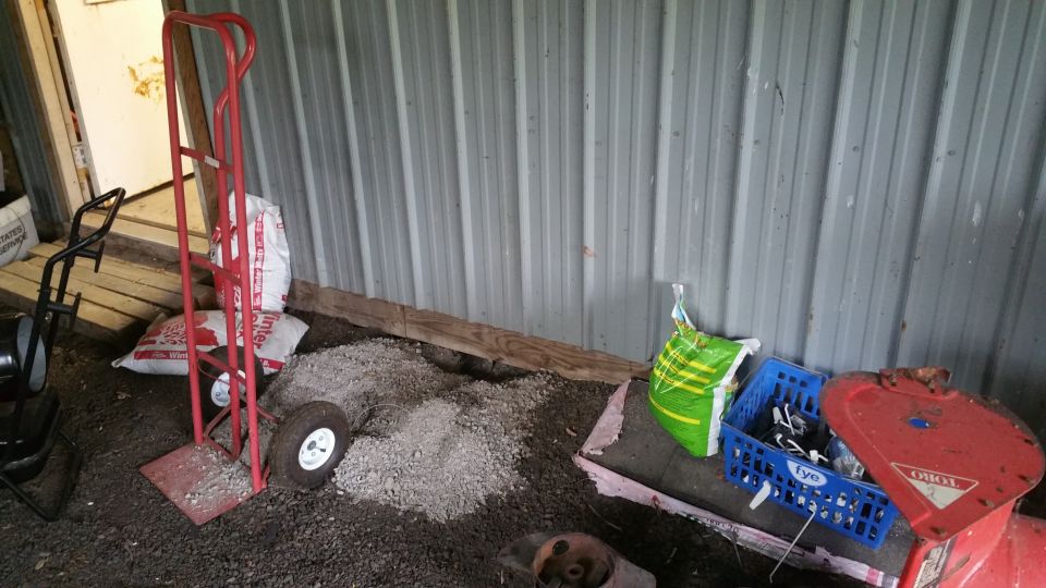 Outdoor storage with bags of material, hand truck, crate, and snow blower.