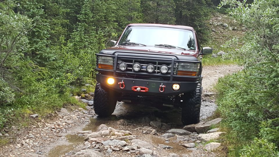 1996 Ford Bronco driving on a rocky, wet trail in a forest.