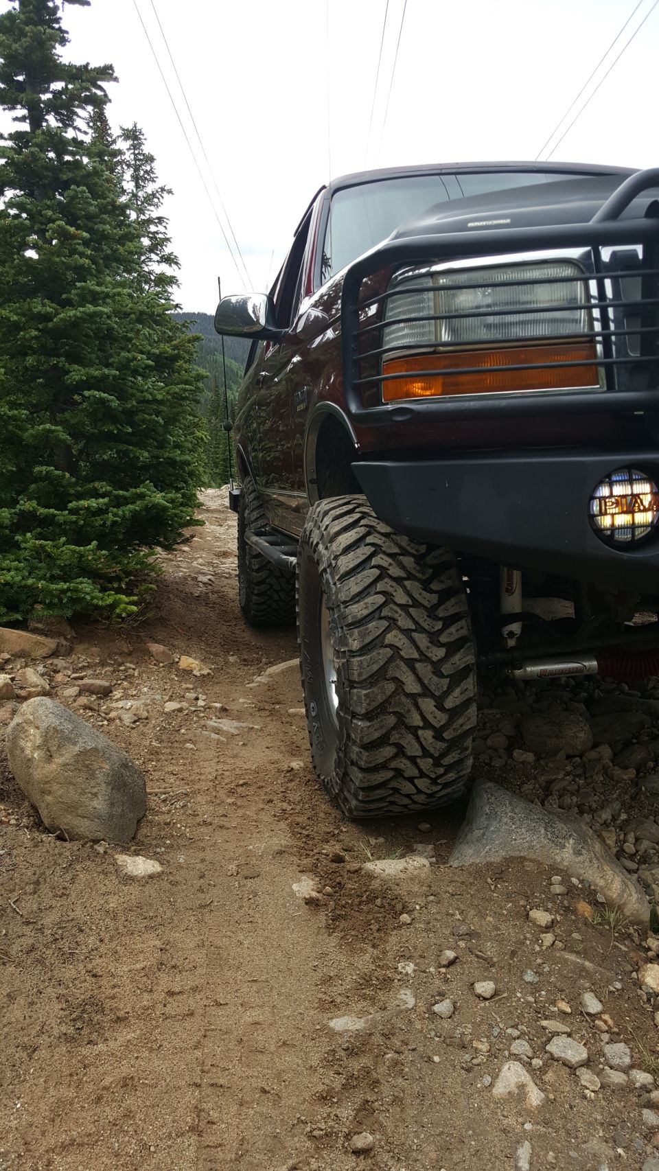 1996 Ford Bronco on a rocky trail with large off-road tires and a brush guard.