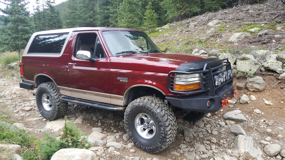 Red 1996 Ford Bronco on a rocky trail with custom bumper and off-road tires.