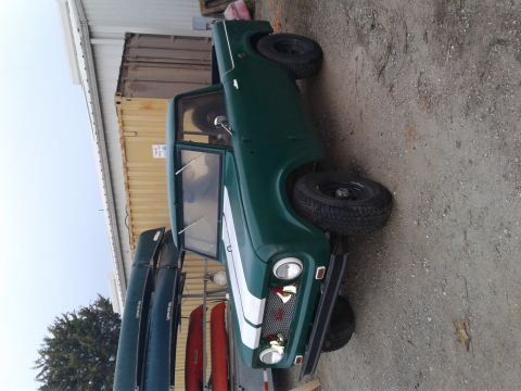 1991 Ford Bronco - A green 1950s-style SUV with a white stripe down the side is parked on a gravel surface next to a shipping container and a building. Severa…