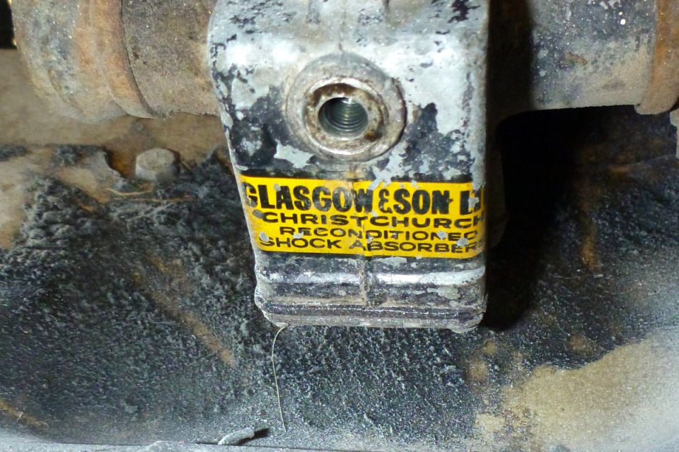 Close-up of a yellow and black label on a shock absorber reading "GLASGOW & SON LTD CHRISTCHURCH RECONDITIONED SHOCK ABSORBER".