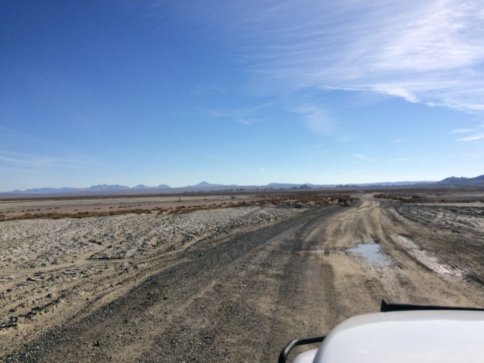 White vehicle on a dirt road in a desert landscape.