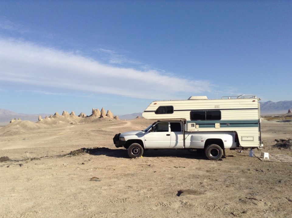 White pickup truck with camper shell parked in desert landscape with rock formations.
