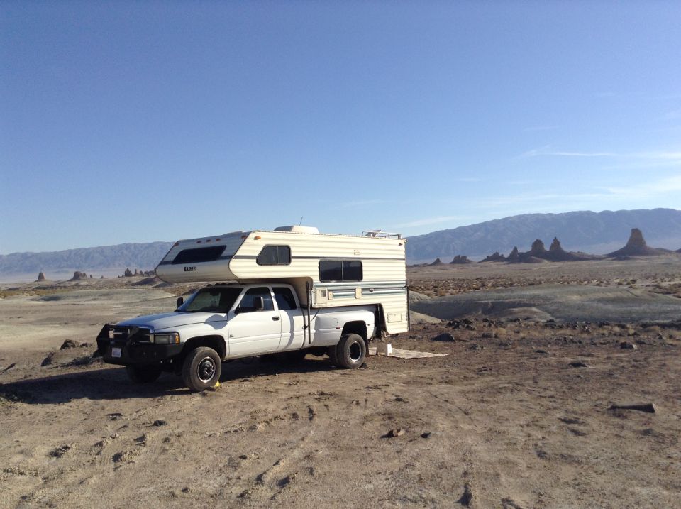 White pickup truck with camper shell parked in a desert landscape.