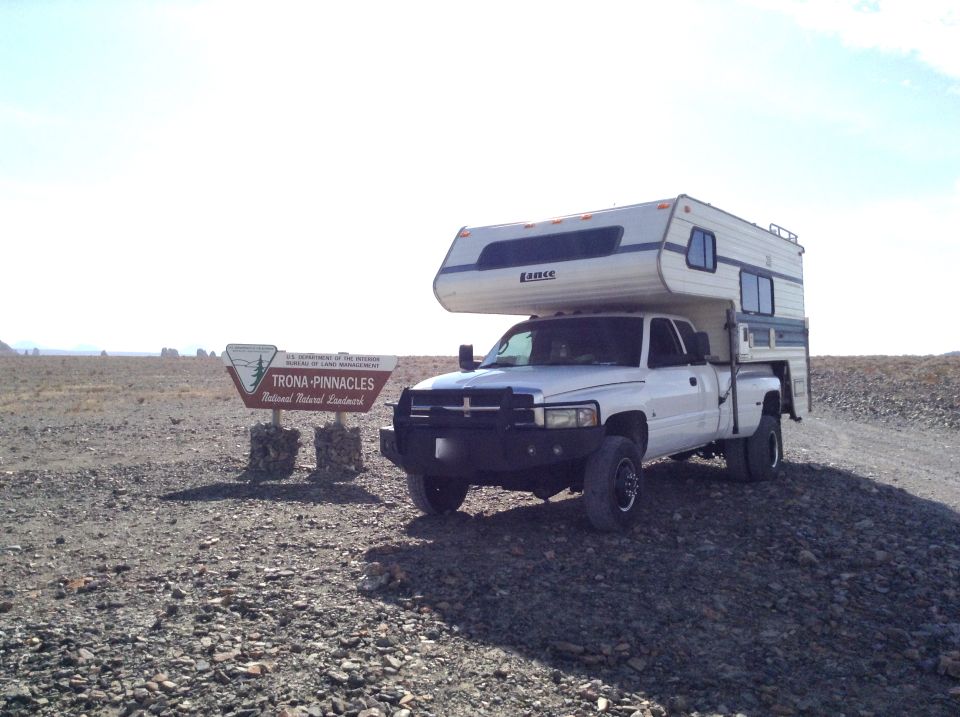 White pickup truck with camper shell at Trona Pinnacles National Natural Landmark sign.