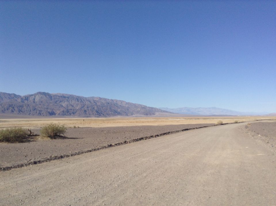 Desert landscape with mountains and a dirt road under a clear blue sky.