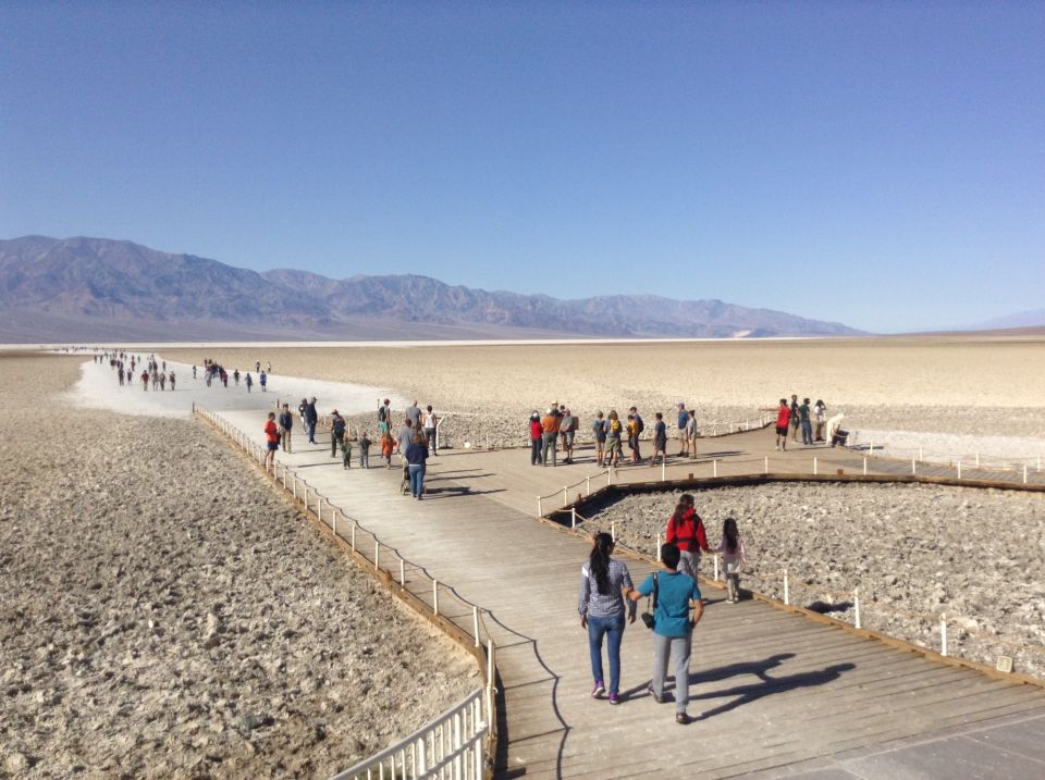 Tourists on a boardwalk in a dry, rocky landscape with mountains in the distance.
