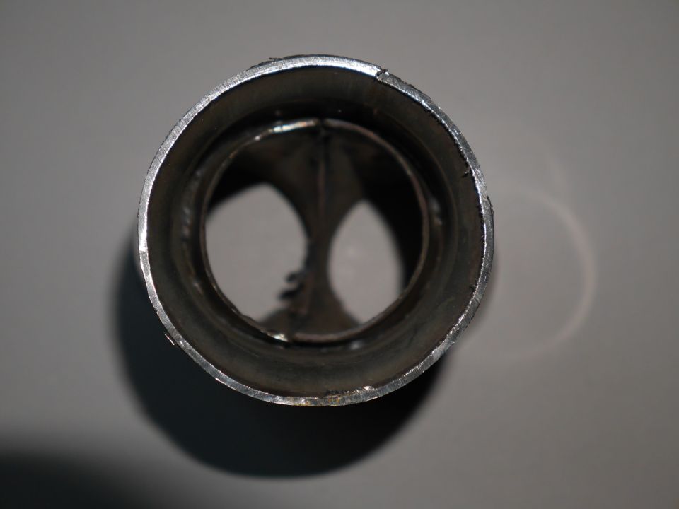 Close-up view into the opening of a metal exhaust pipe, showing internal baffles