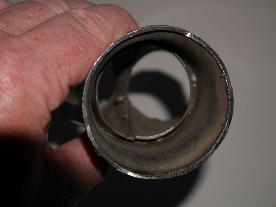 Close-up of a metal pipe held by a hand. The pipe is cylindrical with rough edges