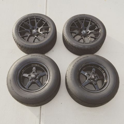 2004 Ford Crown Victoria - A set of four black wheels and tires, two different styles, are displayed against a light-colored wall.