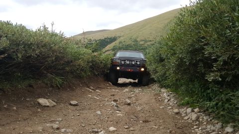 1996 Ford Bronco - A black Ford Bronco navigates a rough, rocky mountain path surrounded by dense foliage.