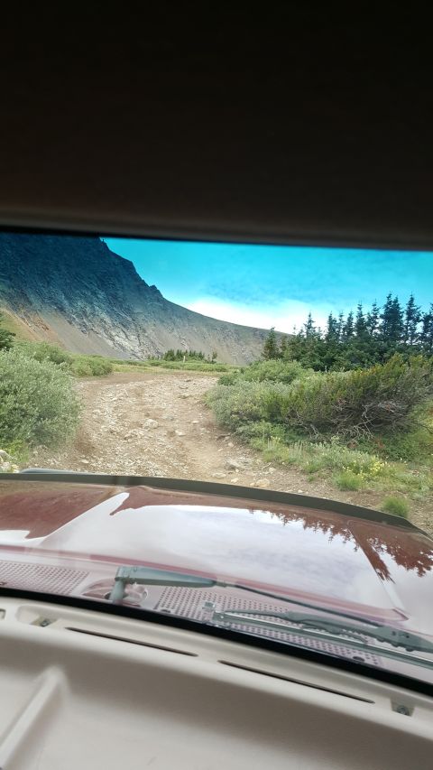 1996 Ford Bronco - View from inside a red vehicle, showing the dashboard and windshield looking out onto a mountain landscape with a dirt road. The Supermotor…