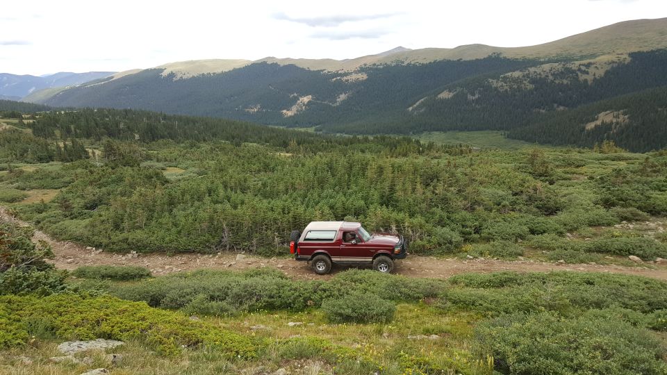 Red Ford Bronco driving on a dirt road in a mountainous, forested area