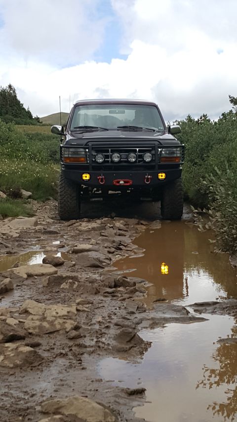 1996 Ford Bronco - This black 1996 Ford Bronco navigates a challenging off-road path with mud and rocks.
