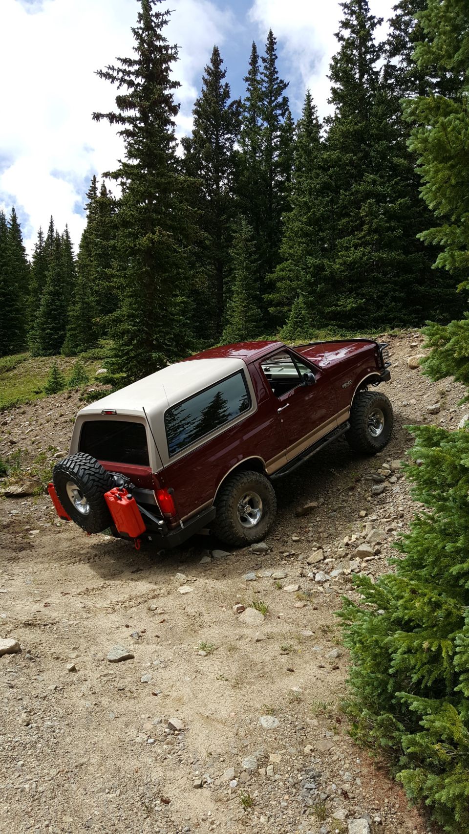 Red 1996 Ford Bronco with spare tire and gas cans on a dirt road