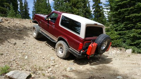 1996 Ford Bronco - A red and white Ford Bronco navigates a steep, rocky incline surrounded by pine trees.