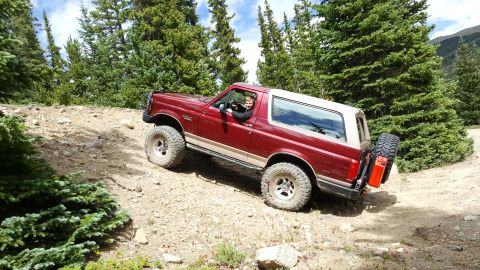1996 Ford Bronco - 1996 Ford Bronco navigates a rocky, uphill trail surrounded by pine trees.