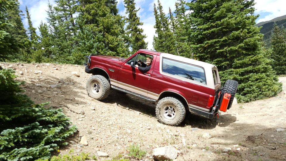 1996 Ford Bronco driving off-road on a dirt path with trees in the background