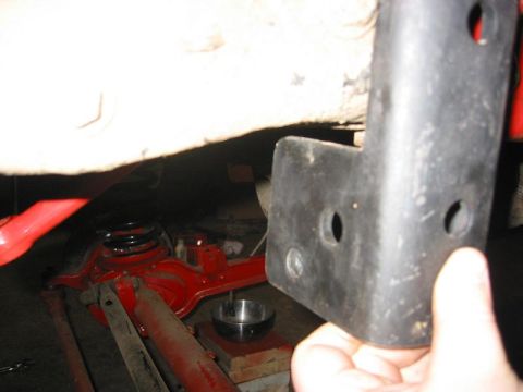1985 Ford Bronco - A black bracket is held near the red suspension components and coil spring of a vehicle.