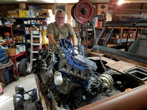 1972 Ford Bronco - Man lowering a V8 engine into a 1972 Ford Bronco during restoration.