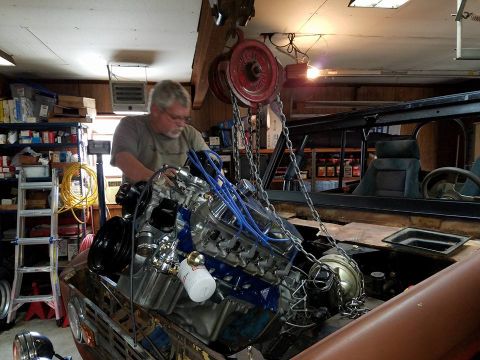 1972 Ford Bronco - Mechanic installs a V8 engine into a vehicle using a hoist in a garage setting.