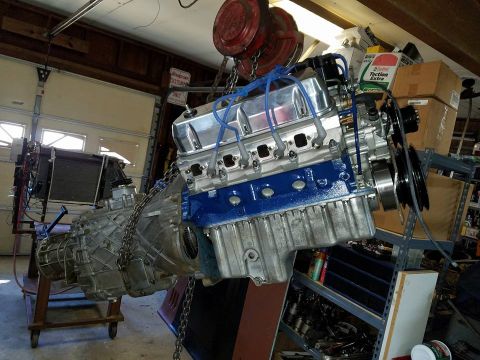 1972 Ford Bronco - Engine and transmission assembly hangs from a hoist in a garage, ready for installation or repair.