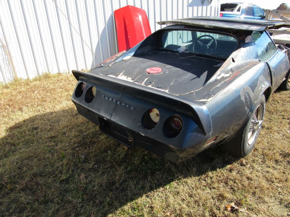 Dark blue Chevrolet Corvette, rear view, missing taillights and bumper, peeling paint, aftermarket spoiler