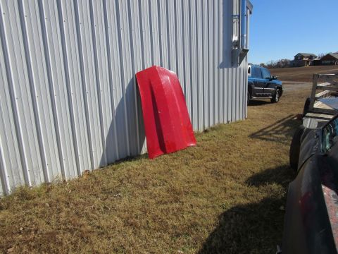 Red car hood leaning against a corrugated metal building wall