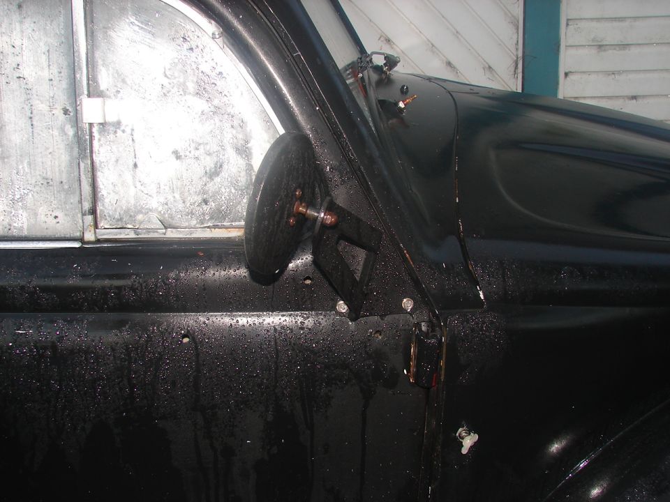 Black 1964 Volkswagen Beetle door and side mirror, wet surface, close-up
