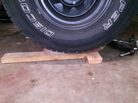 1996 Ford Bronco - A close-up view of a large tire resting on wooden blocks. The tire has white lettering that reads "DISCOVERER" and "PER".