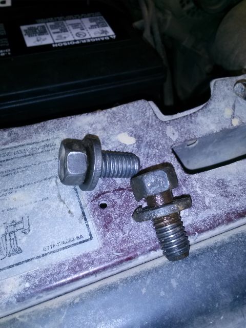 1996 Ford Bronco - Two metal bolts with hex heads and integrated washers are shown resting on a dusty surface. One bolt is larger and appears cleaner than the…