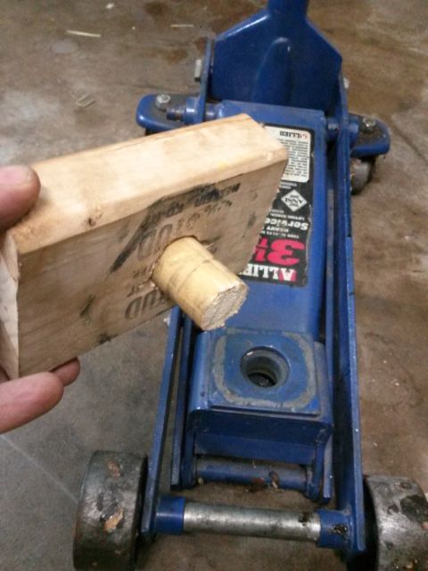 1996 Ford Bronco - A person is holding a wooden block with a dowel inserted into it, about to place it on a blue hydraulic floor jack. The jack has a label th…
