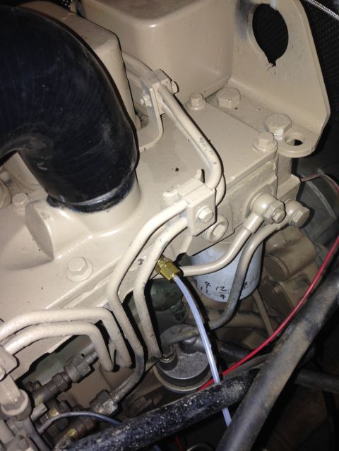 1994 Ford Bronco - Close-up view of a tan-colored engine block with various fuel lines and a fuel filter. A black intake hose is visible on the left.