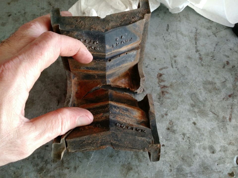 Close-up of a broken, rusty, black metal vehicle part with embossed text.