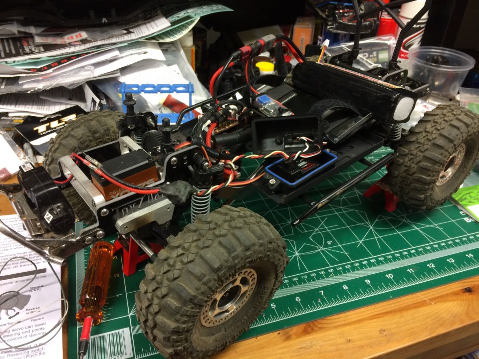 RC rock crawler vehicle disassembled on a green cutting mat with tools and instructions.