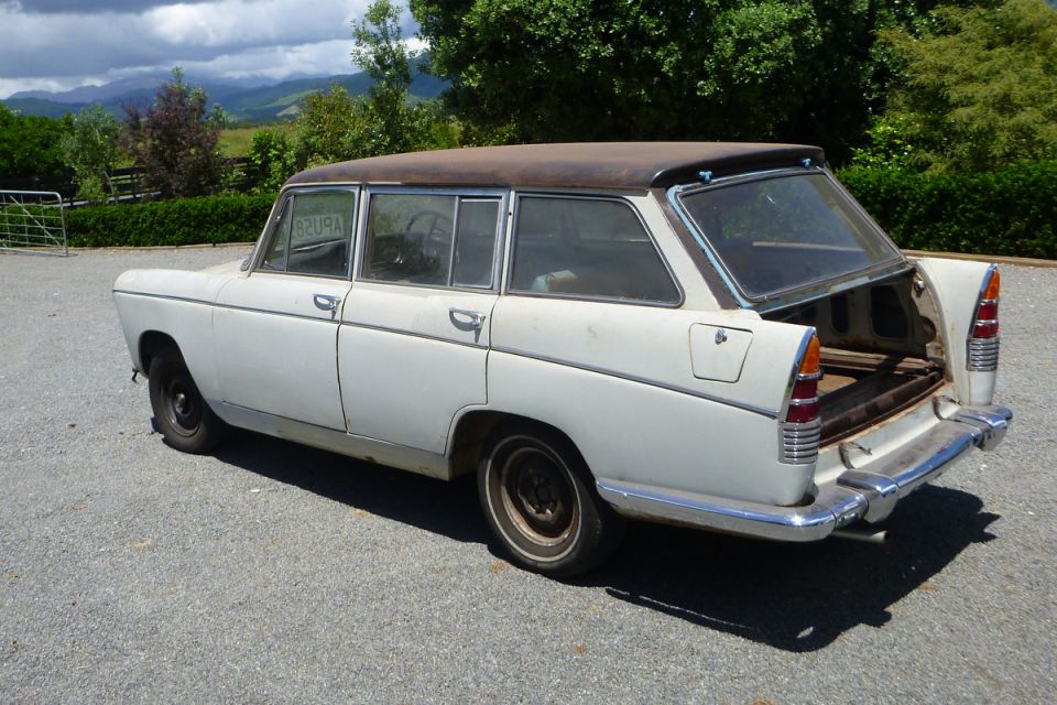 White vintage station wagon with rusty roof, rear-left view, open hatch.
