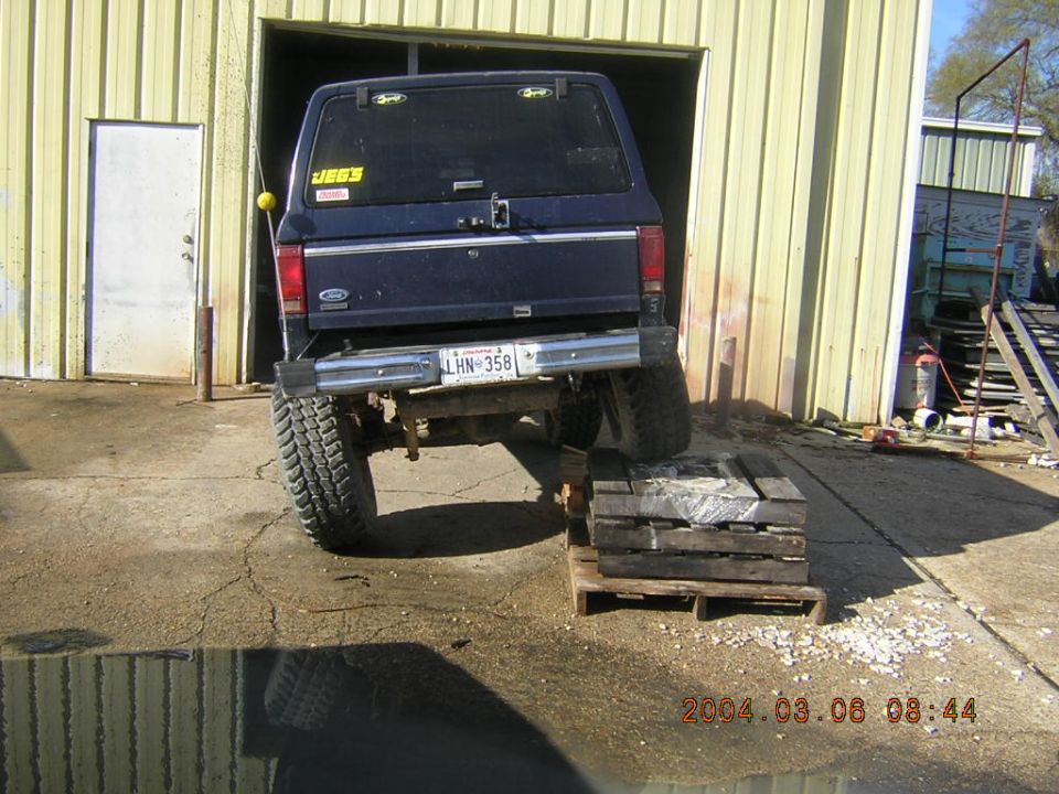 Dark blue SUV rear, lifted with large tires, on wooden blocks. License plate LHN-358