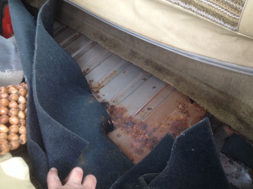 Rusty floor of a vehicle with dark blue carpet being lifted.