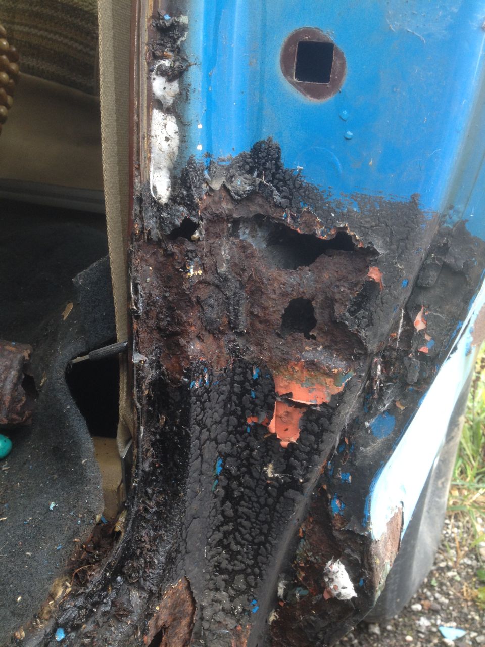 Close-up of severe rust damage on the lower door jamb of a blue vehicle.
