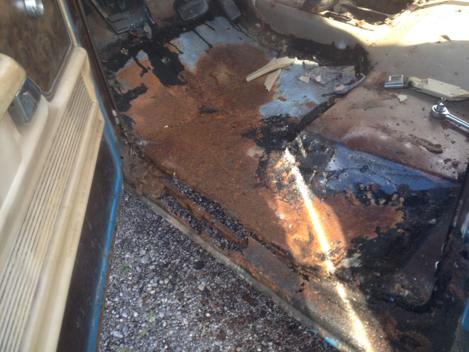 Rusted out interior floor of a vehicle with door panel visible.