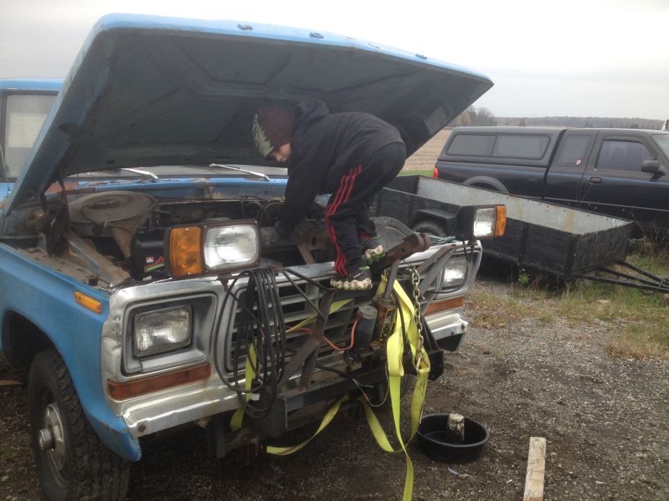 Person working on the engine of a blue classic Ford truck.