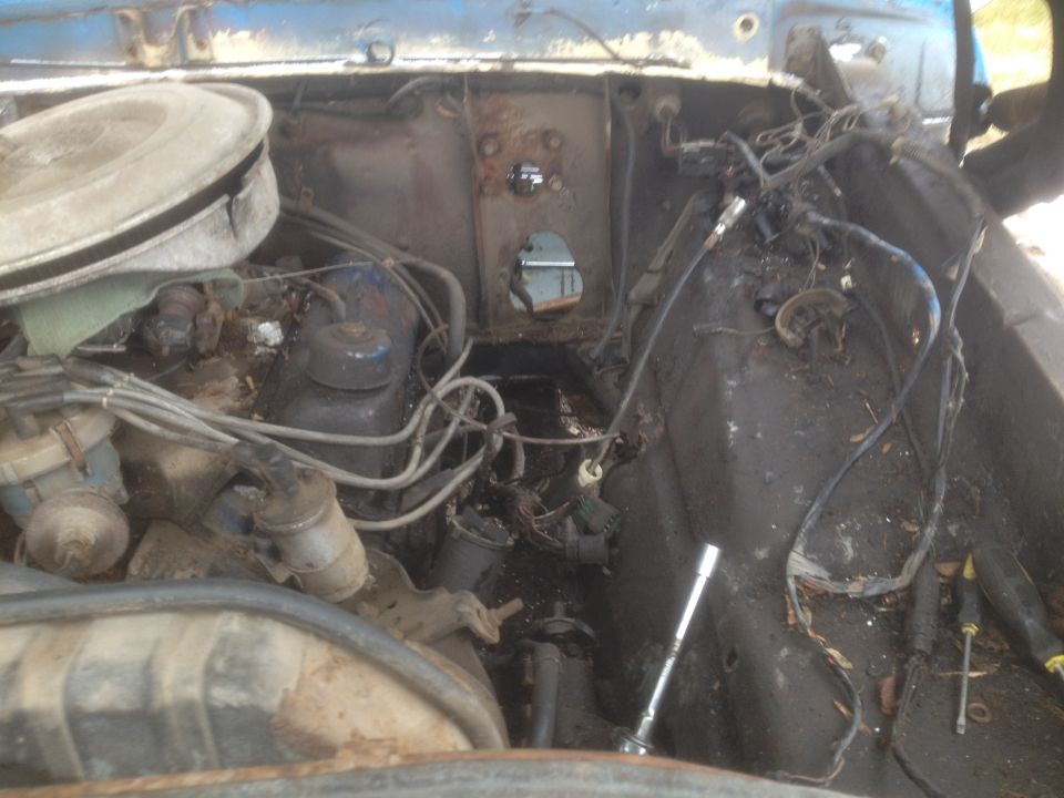 Engine bay of a vintage Ford Bronco with engine parts, wiring, and a socket wrench.