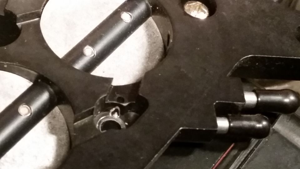 Close-up of a black mechanical part with silver pins and black cylindrical ends.