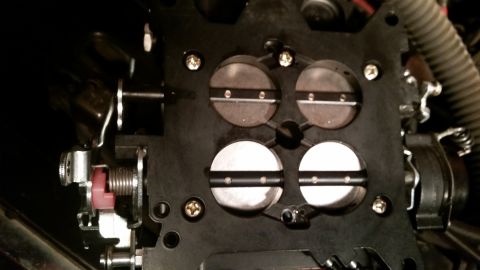 1981 Ford Bronco - A close-up view of the throttle body of a vehicle, showing four circular throttle plates with metal bars across them. The throttle body is…