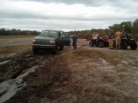 1996 Ford Bronco - A dark green 1990s Ford Bronco with the driver's door open sits in a muddy, rutted area next to several ATVs and a group of people. The Bro…