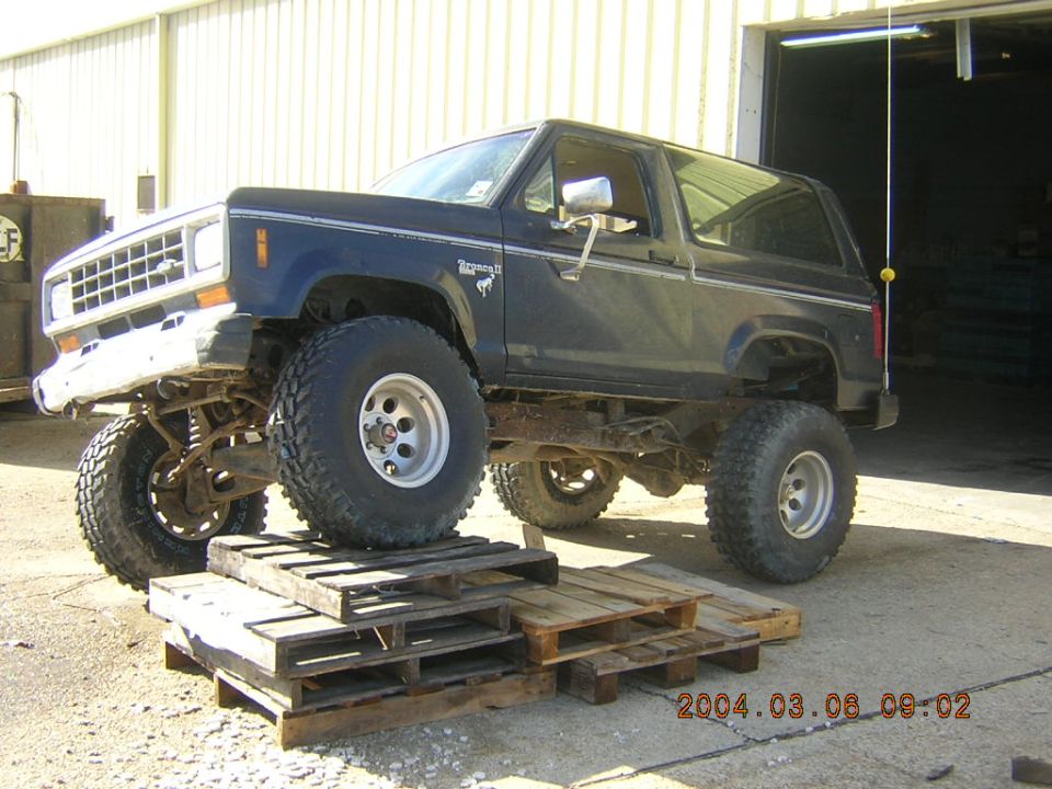 Lifted 1980s Ford Bronco II with large tires, front end elevated on wooden pallets
