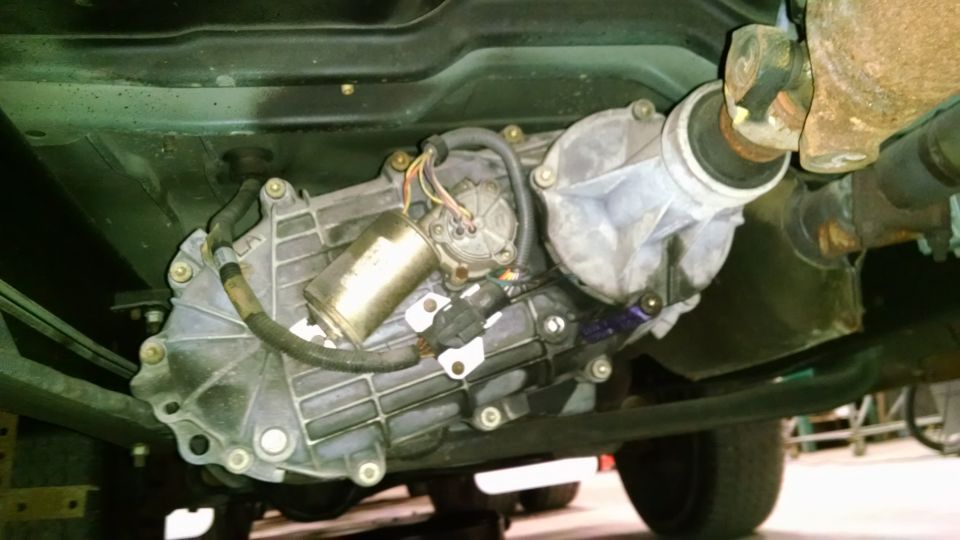 Underneath view of a vehicle's transfer case and driveshaft components.