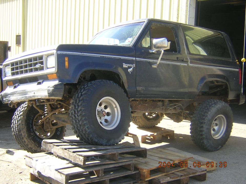 Dark blue Ford Bronco II lifted with large tires, sitting on wooden pallets
