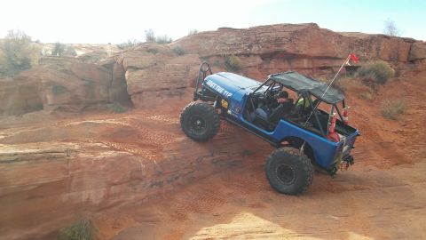1979 Ford Bronco - A custom blue off-road vehicle navigates a steep, sandy incline in a desert landscape.